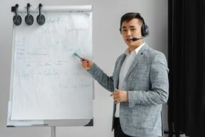 Asian man in a gray suit giving a presentation with a flipchart, wearing a headset.